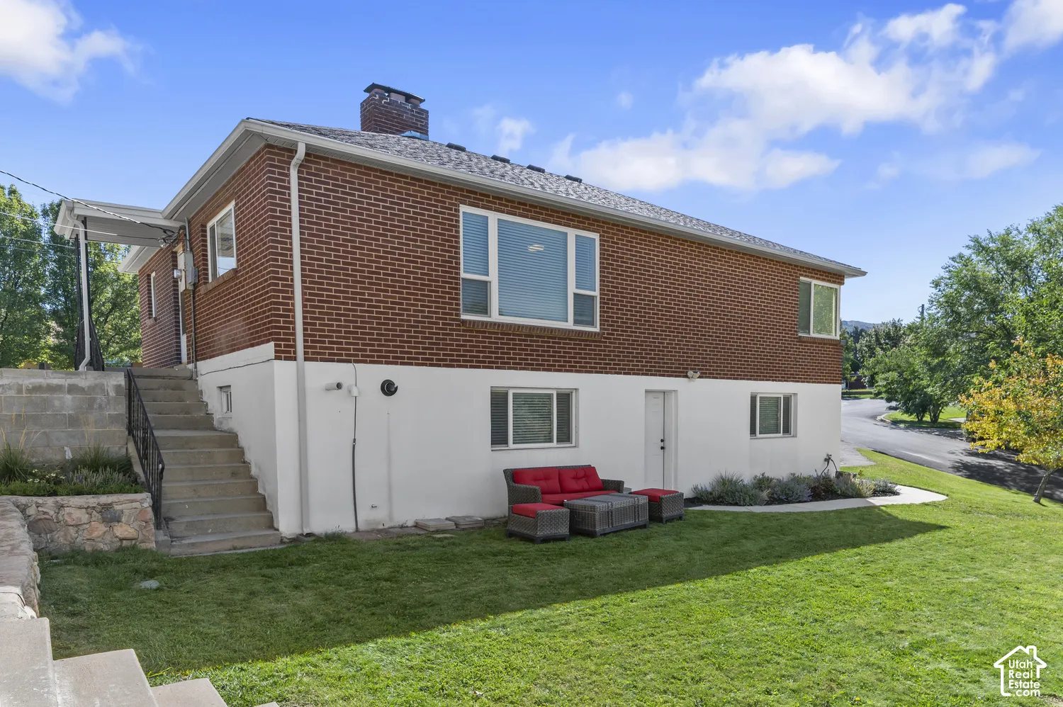 Brick exterior with white lower level, multiple windows, asphalt shingle roof, and a concrete staircase with a metal railing