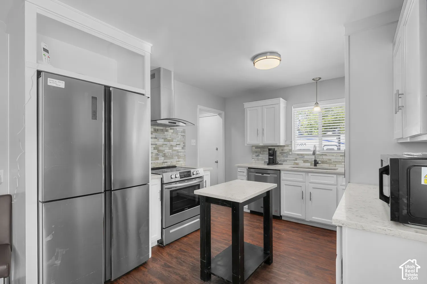 Stainless steel appliances, white cabinetry, wood-finish flooring, mosaic tile backsplash, and light-toned countertops