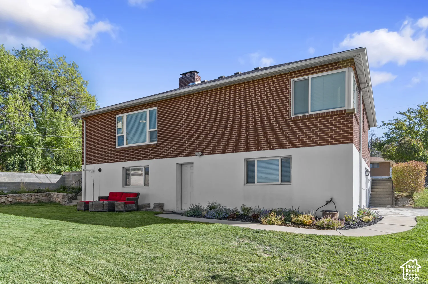 Brick and white exterior with multiple windows, leading to a lawn with landscaping