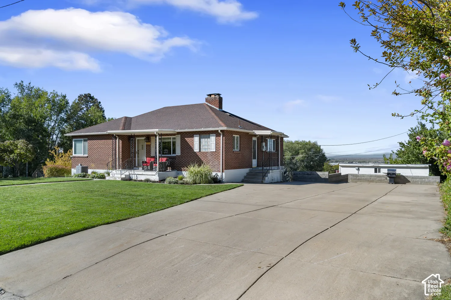 Brick exterior residence featuring a covered front porch, expansive concrete driveway, and a spacious lawn