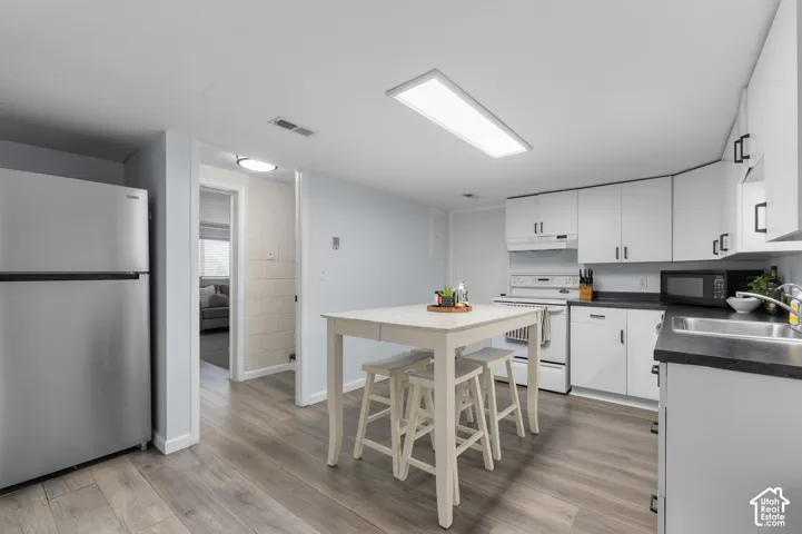 Kitchen featuring white cabinetry, dark countertops, a stainless steel refrigerator, and wood-finish flooring