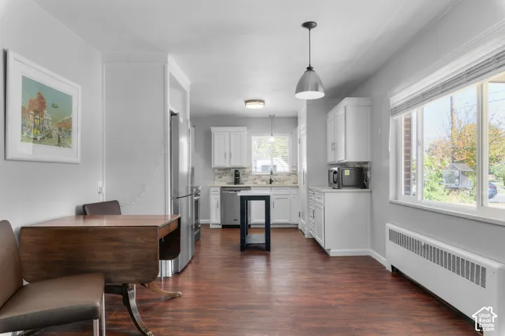 Open-concept kitchen and dining area featuring wood-finish flooring, white cabinetry, stainless steel appliances, and a tiled backsplash