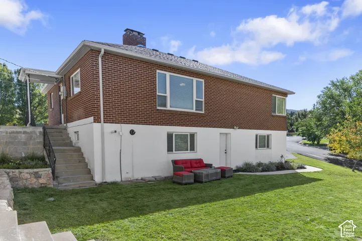 Brick exterior with white lower level, multiple windows, asphalt shingle roof, and a concrete staircase with a metal railing