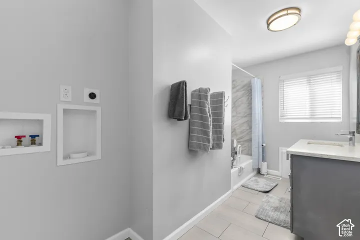 Integrated laundry hookups, tiled flooring, white window blinds, full bathroom with bathtub, and single vanity with a white countertop