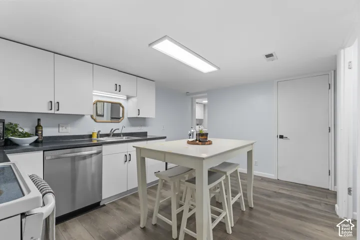 Kitchen featuring white cabinetry with dark hardware, dark countertops, a stainless steel dishwasher, and wood-finish flooring