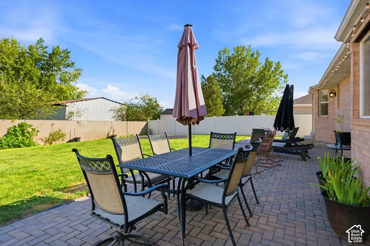 Brick paver patio with a dining area, manicured lawn, and privacy fencing
