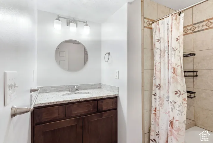 Bathroom vanity with a granite-style countertop, undermount sink, dark wood-finish cabinetry, and a round mirror
