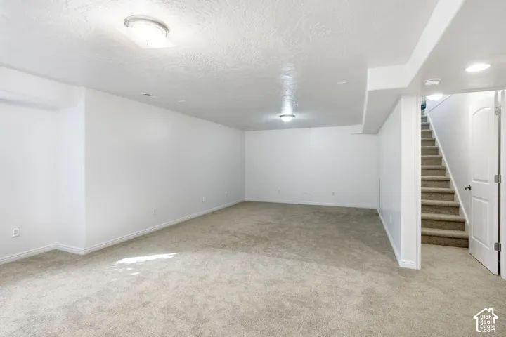 Open-plan room featuring neutral carpeting, white walls, flush-mount lighting, and a staircase with a paneled door