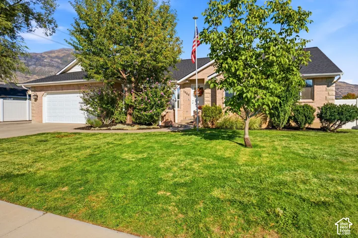 Brick facade, attached garage, dark shingle roof, established landscaping, and mountain backdrop