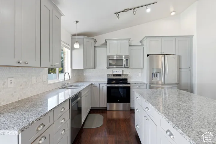 Kitchen featuring light gray cabinetry, stainless steel appliances, speckled countertops, and a white hexagonal tile backsplash