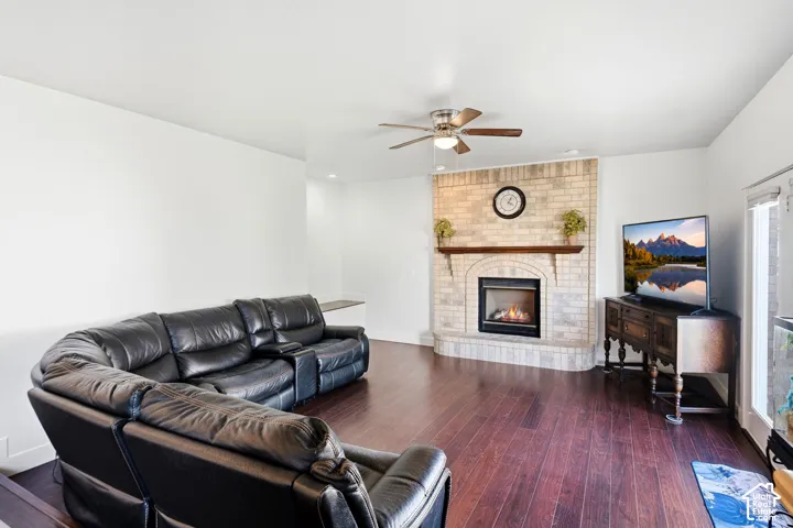 Living area featuring wood-finish flooring, a corner brick fireplace with a wood mantle, and a ceiling fan