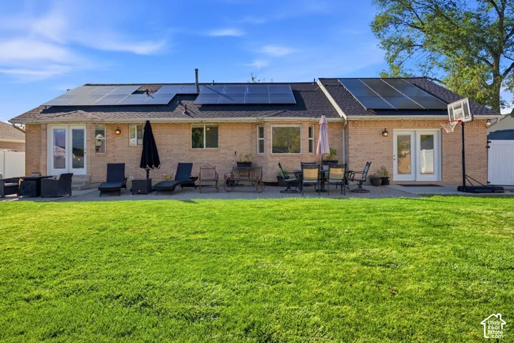 Brick exterior with multiple solar panel arrays, a large patio space, and two sets of double French doors