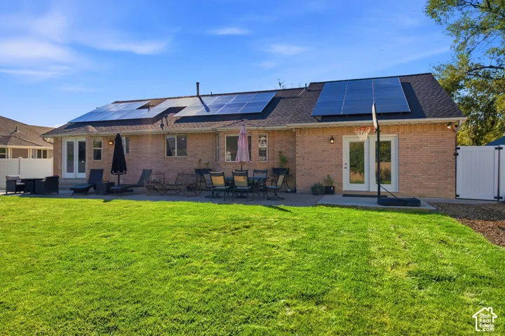 Expansive backyard featuring a large paved patio, solar panels, and brick exterior