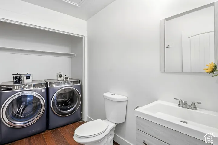 Compact laundry area with built-in shelving, wood-finish flooring, white vanity with integrated sink, and wall-mounted mirror
