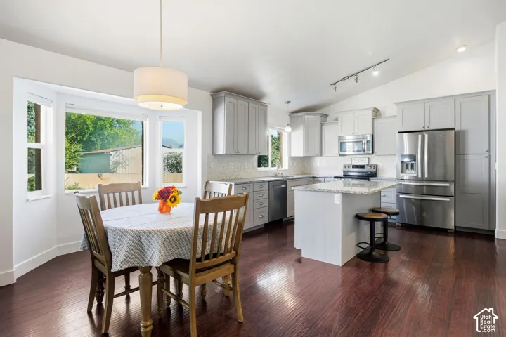 Open-concept kitchen and dining area featuring stainless steel appliances, white cabinetry with gray accents, quartz countertops, a white kitchen island with seating, and rich wood-finish flooring throughout