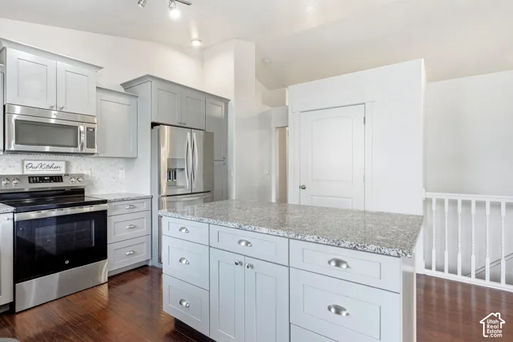 Kitchen featuring a center island with light granite countertops, stainless steel appliances, shaker-style cabinetry, and wood-finish flooring