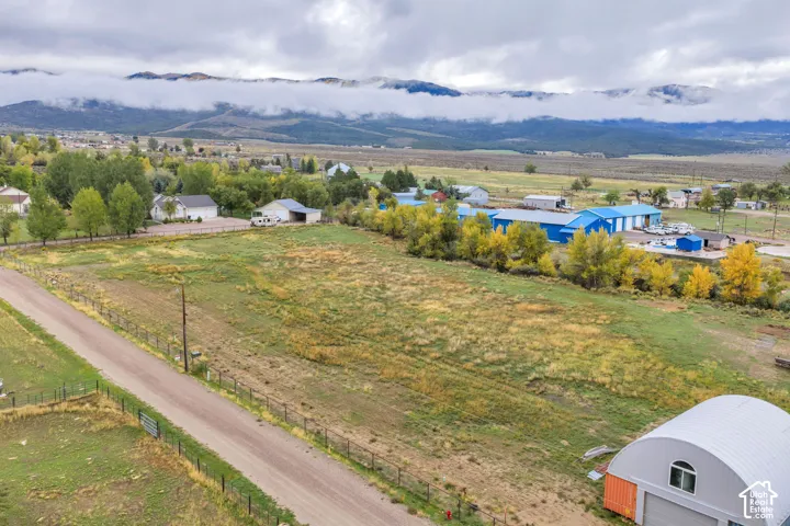 Expansive open land featuring a gravel road, partial fencing, distant mountains, and scattered trees