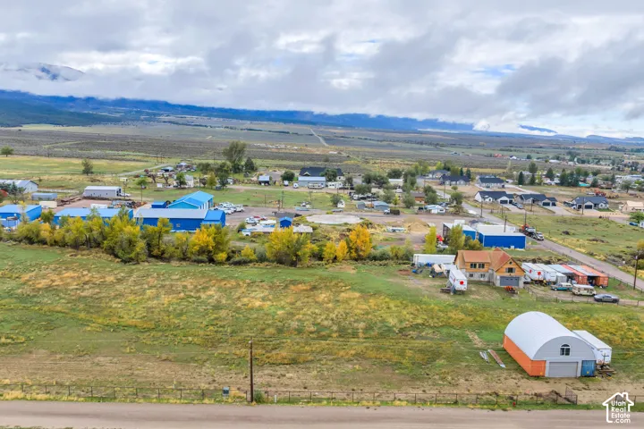 Expansive rural landscape featuring a mix of residential structures and commercial-style buildings, with distant mountains under a cloudy sky