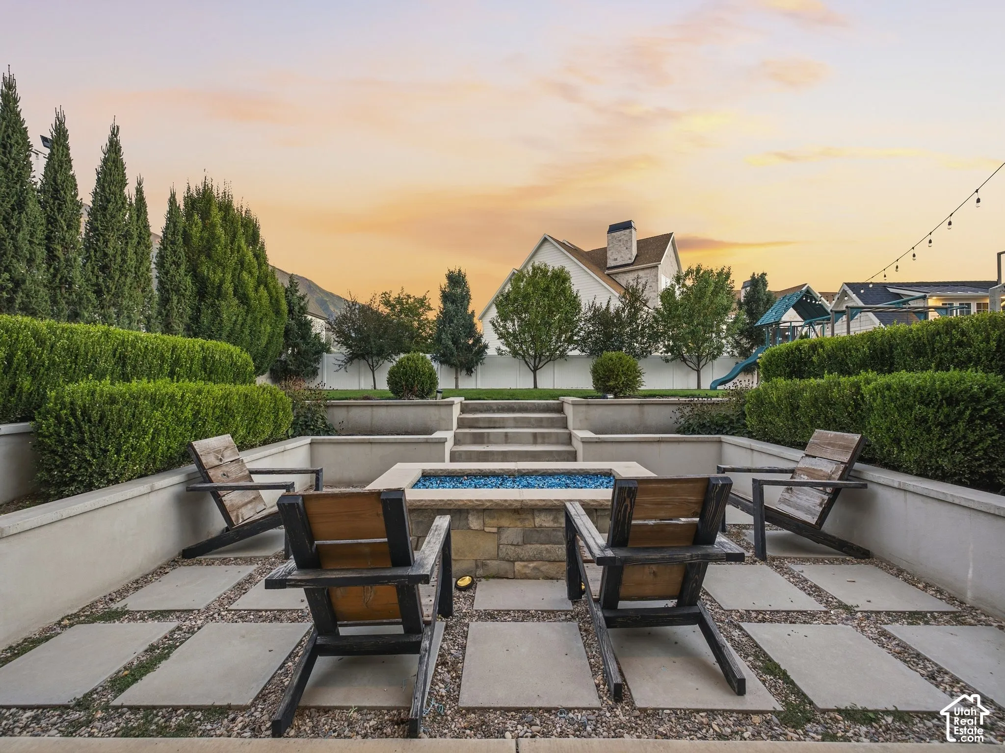 Multi-level terraced patio featuring a stone fire pit with blue fire glass, concrete pavers, and decorative gravel