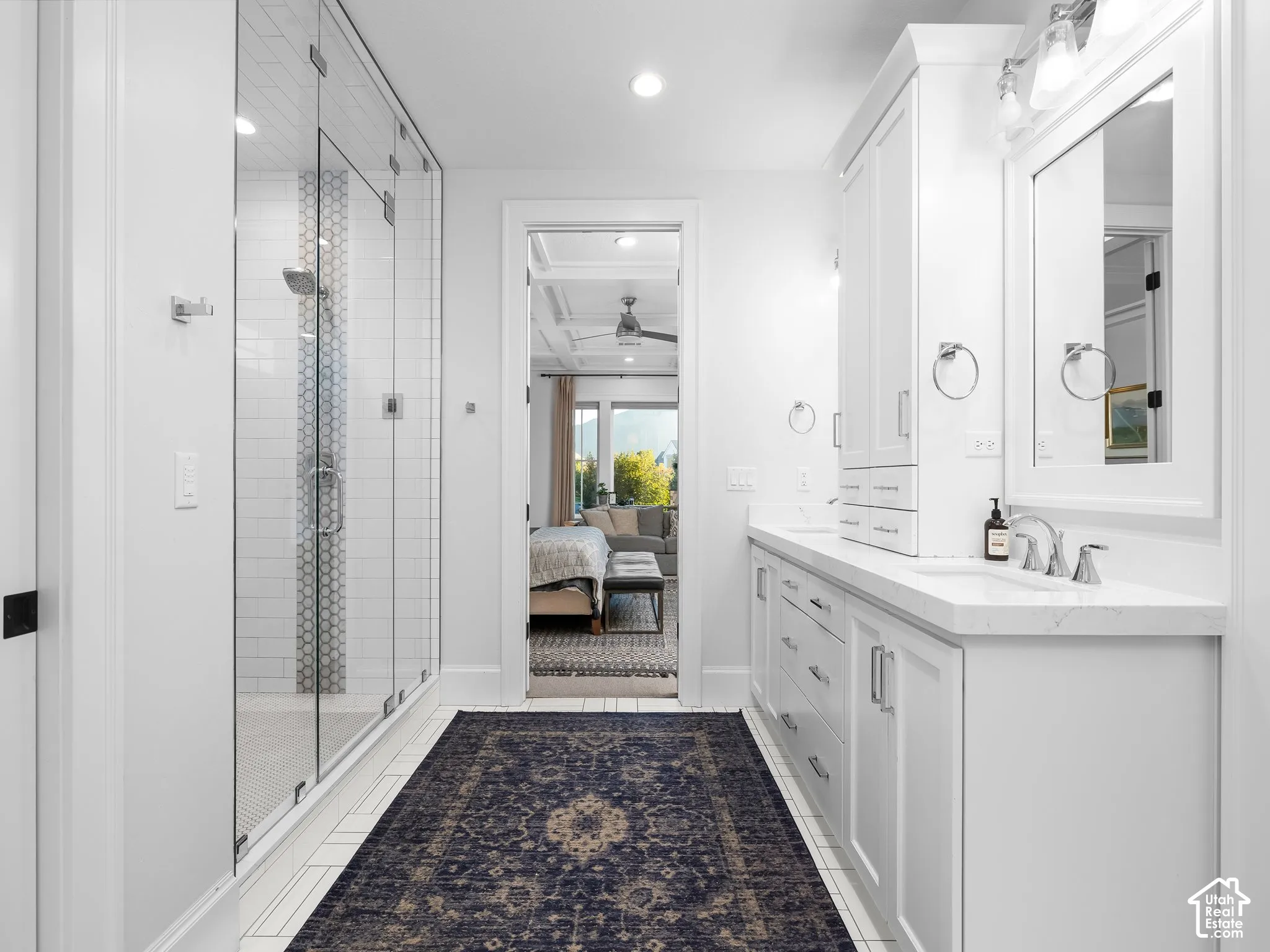 Spacious bathroom featuring a frameless glass shower, dual vanities with white cabinetry, polished chrome fixtures, and a white countertop