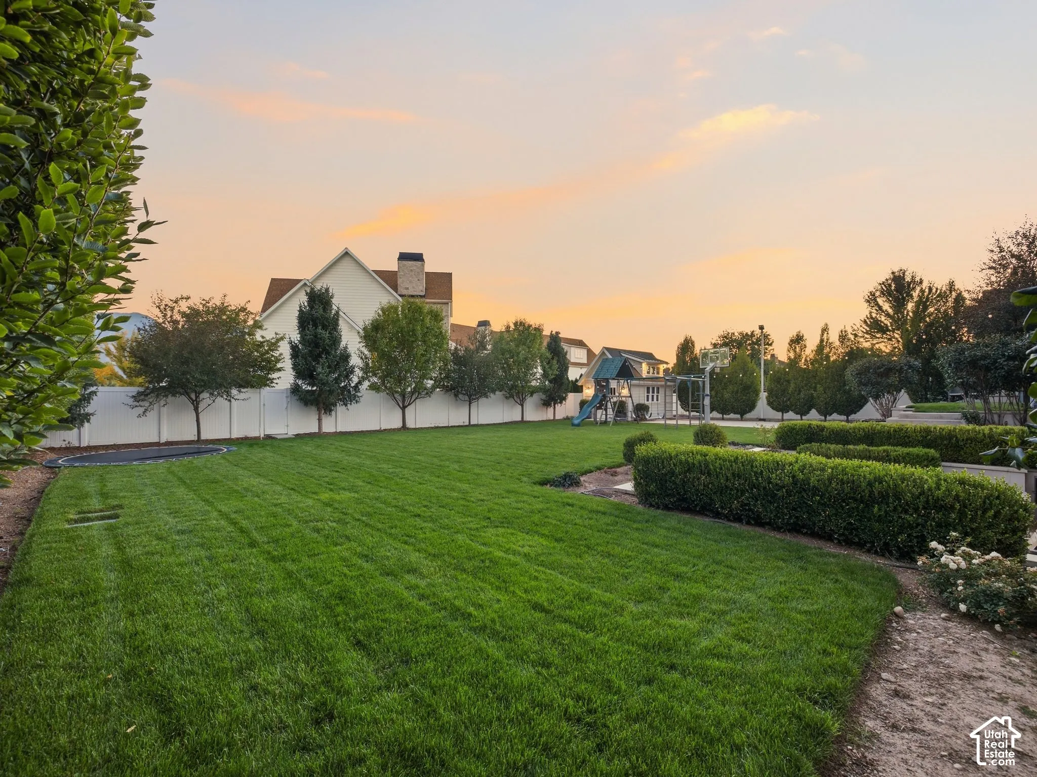Expansive green lawn with mature trees, shrubbery, and a white privacy fence