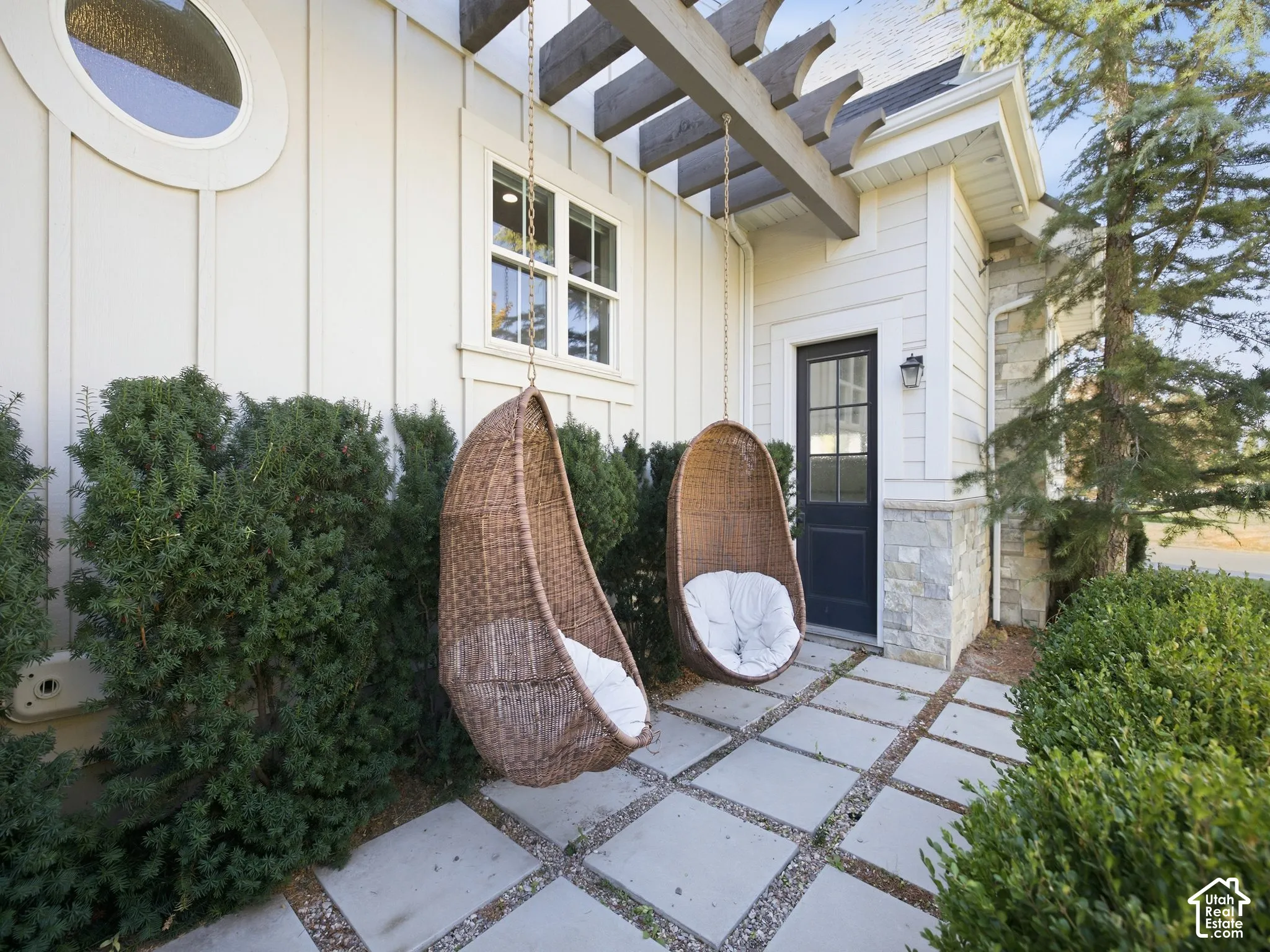 Exterior featuring a pergola structure, stone and vertical siding, a round window, and square paver patio