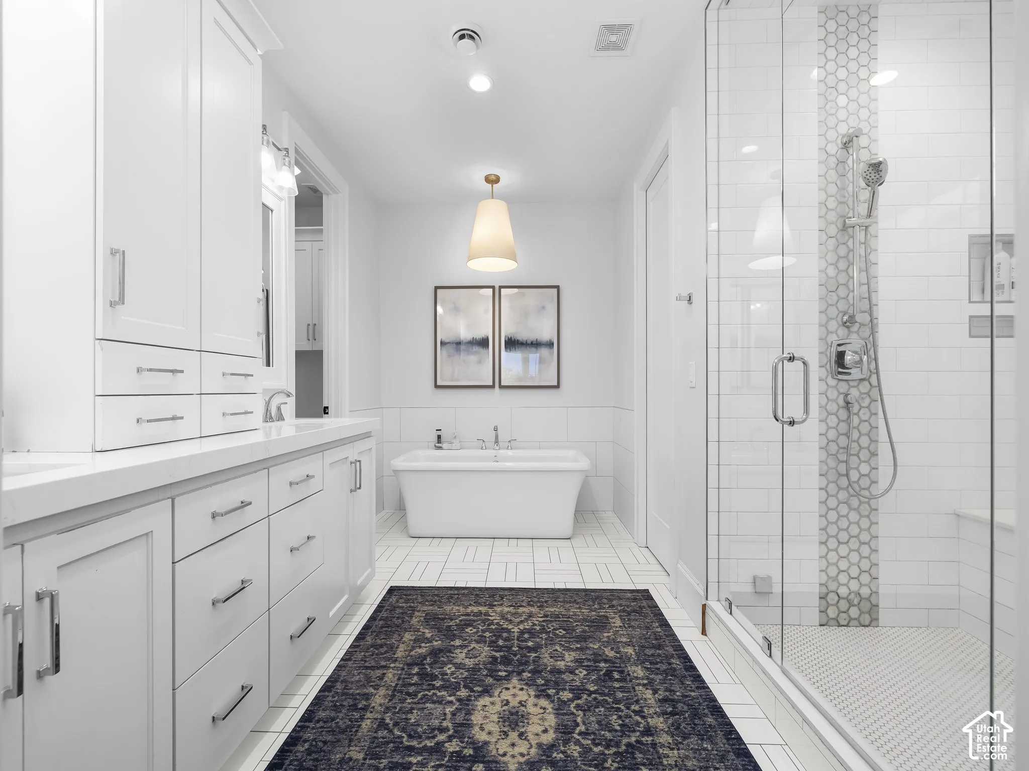 White cabinetry with chrome hardware, freestanding soaking tub, glass-enclosed shower, white subway tile, and hexagon tile accents