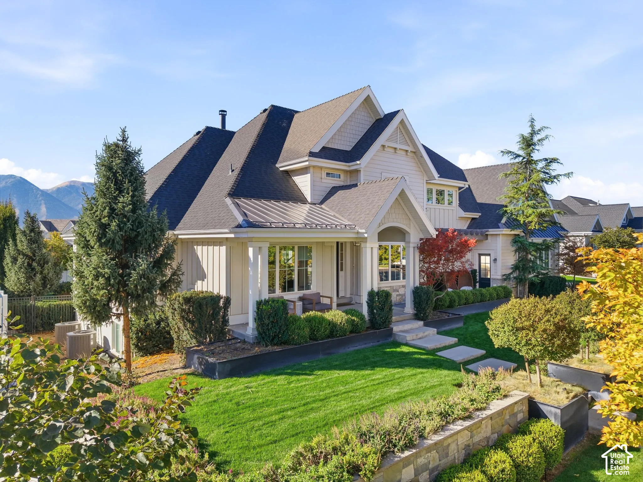 Gable roofline with dormer windows, stone and siding exterior, covered entry porch, manicured lawn, and multi-level landscaping