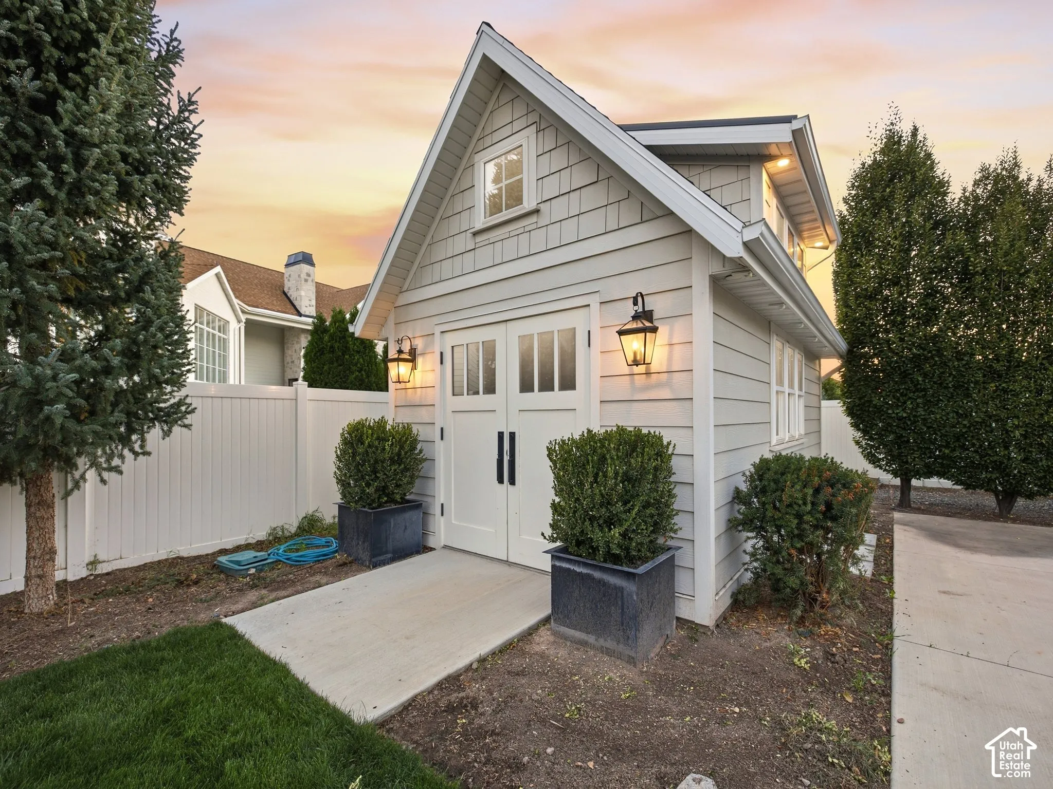 Gabled-roof outbuilding with shake and horizontal siding, featuring double doors with glass panes, transom window, and exterior wall sconces