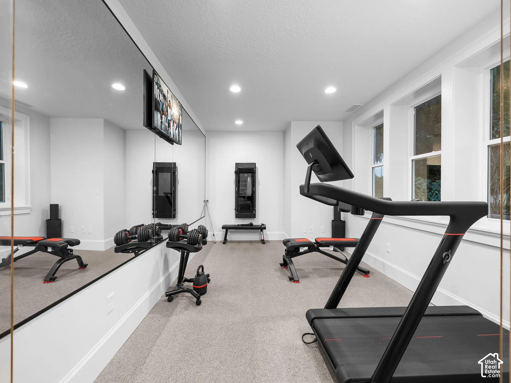 Recessed lighting illuminates this space featuring a full wall mirror, multiple windows, and light-toned carpeting