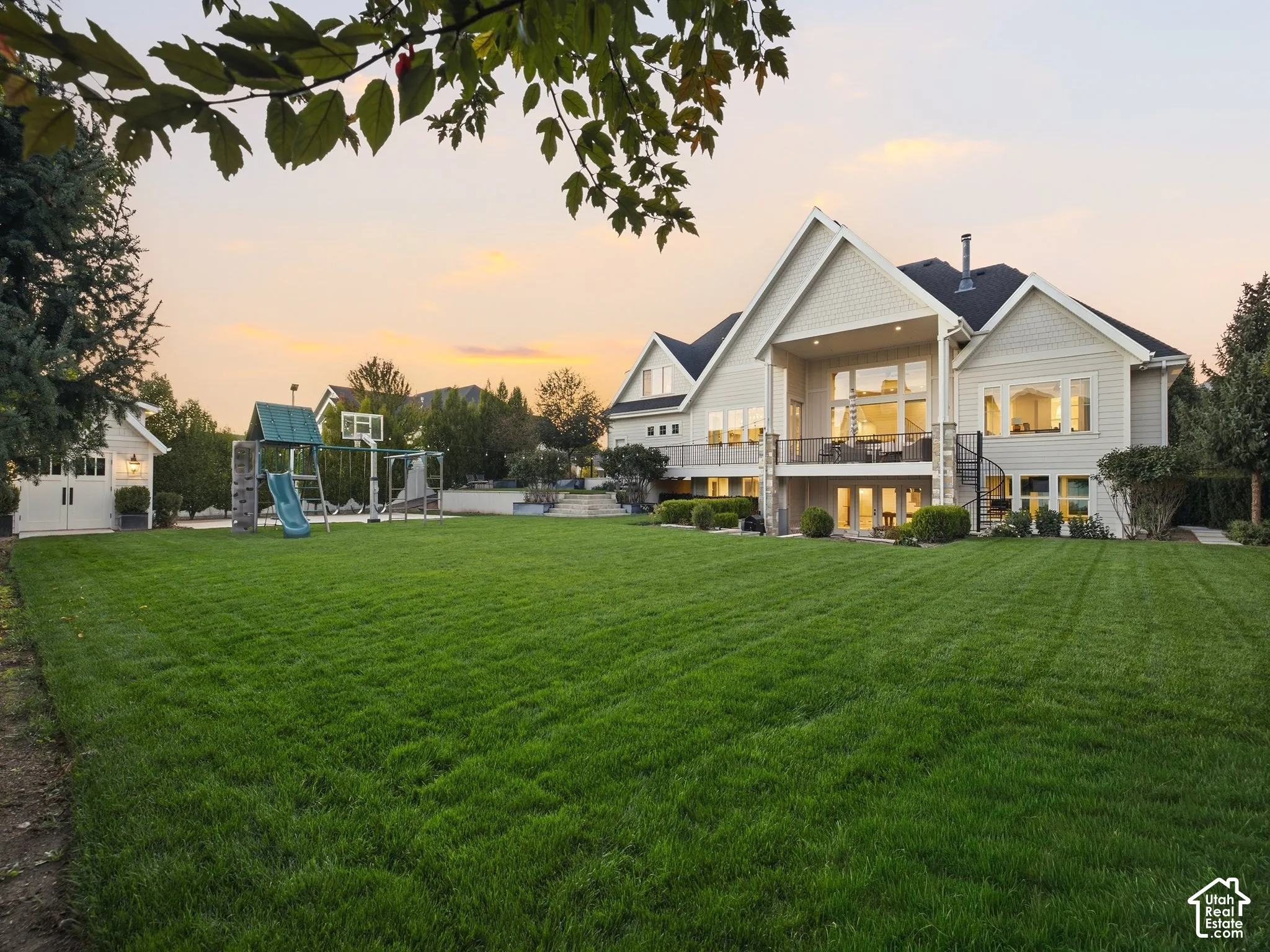 Expansive rear lawn with a two-story home, a covered upper-level deck, lower-level patios, and an exterior spiral staircase