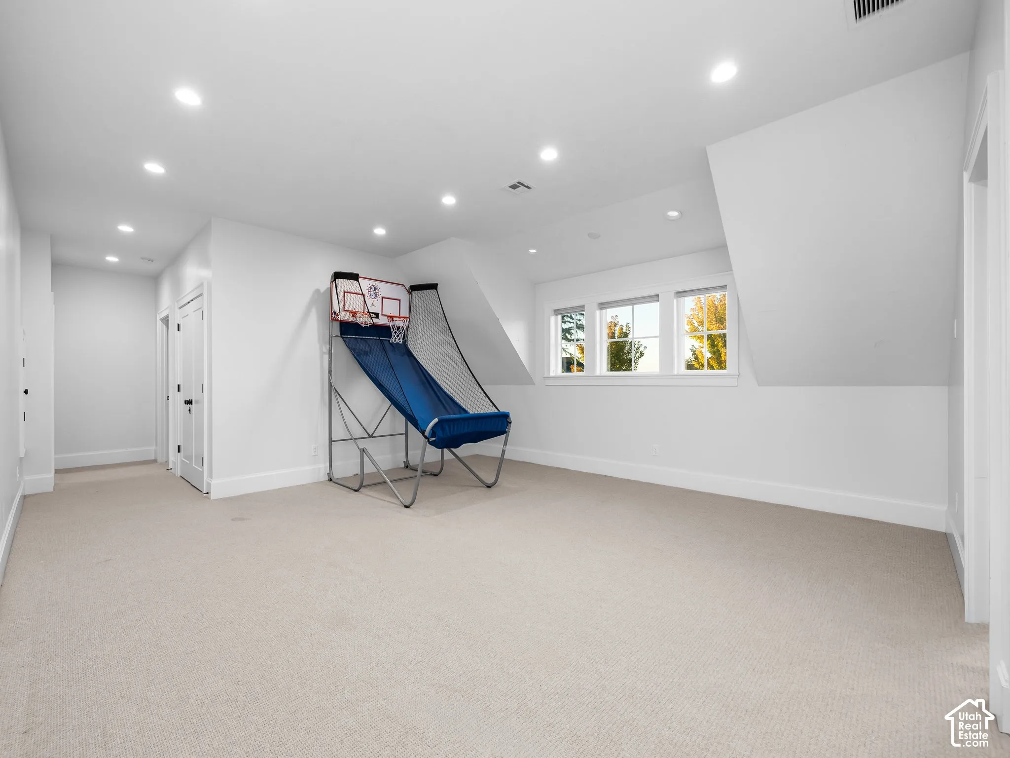 Spacious room featuring carpeting, recessed lighting, white walls, multiple windows, and a sloped ceiling