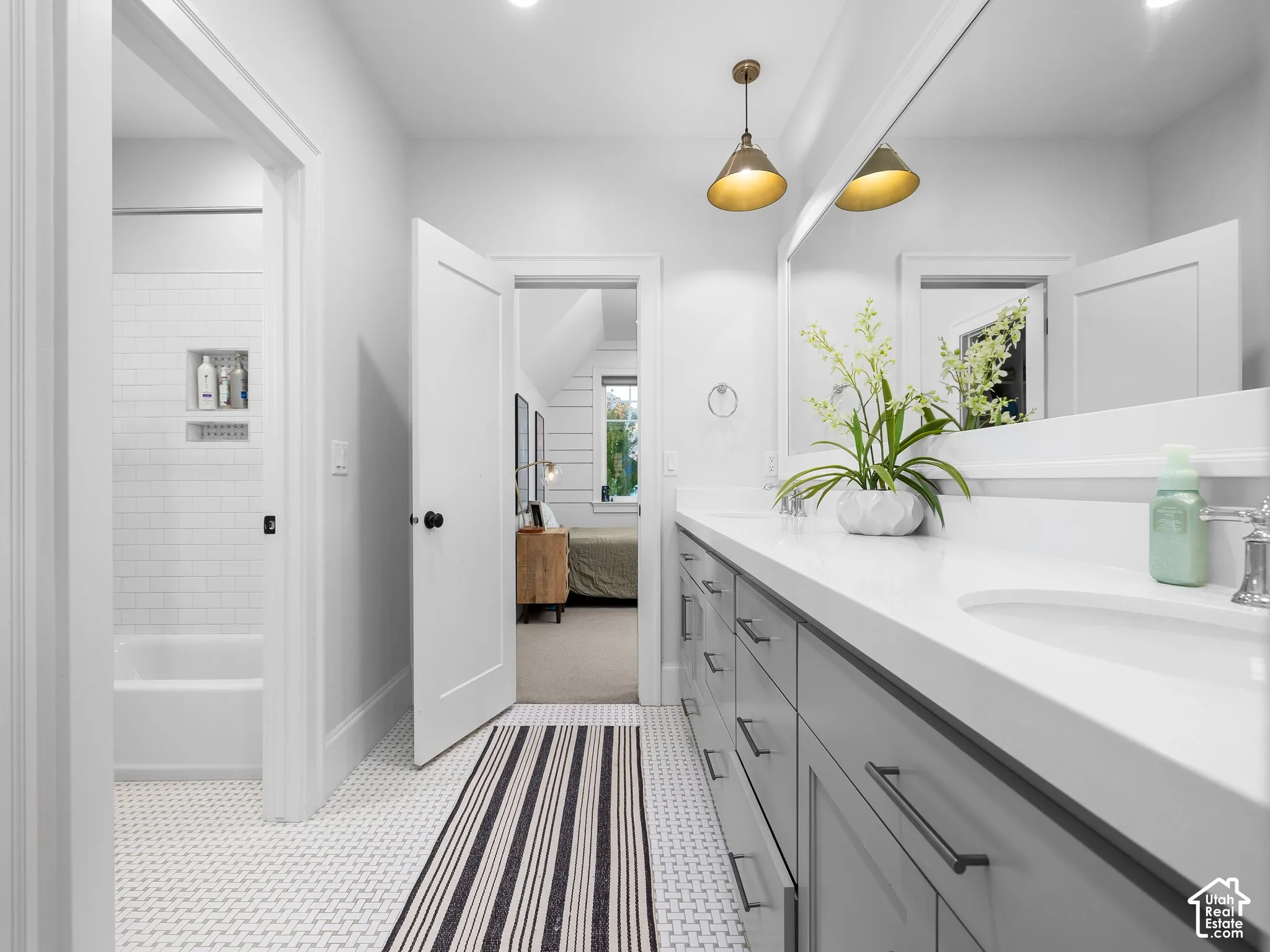 Double vanity with a white countertop and integrated sinks, gray shaker-style cabinetry with matte black hardware, and two brass-finish pendant lights