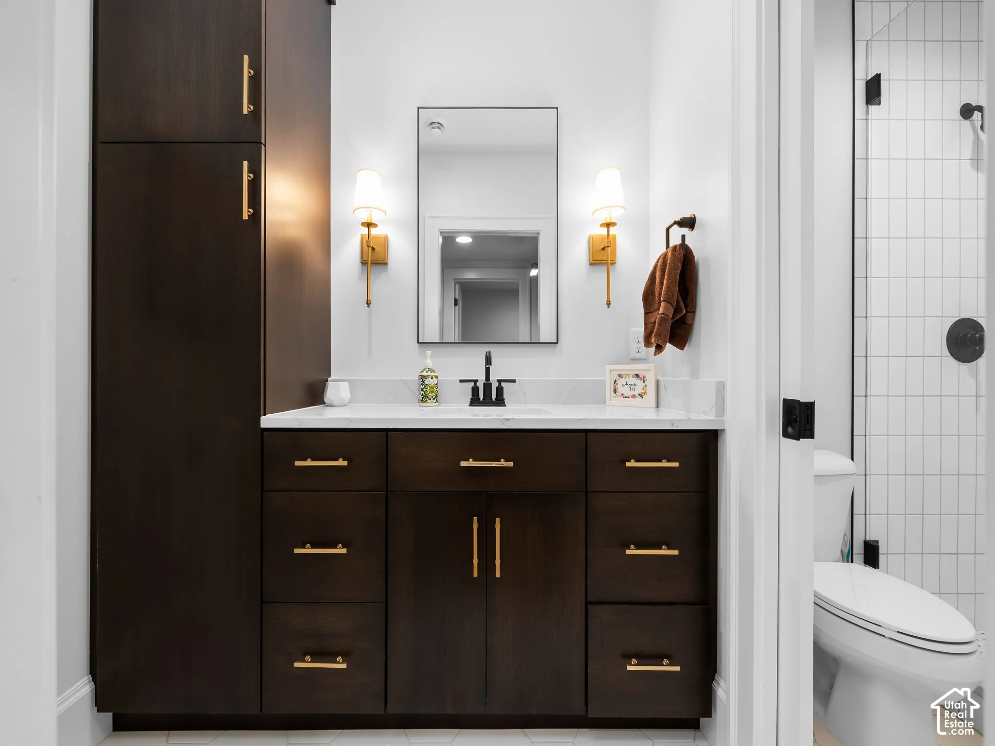 Dark wood-finish cabinetry, white countertop, rectangular vanity mirror, and dual sconce lighting
