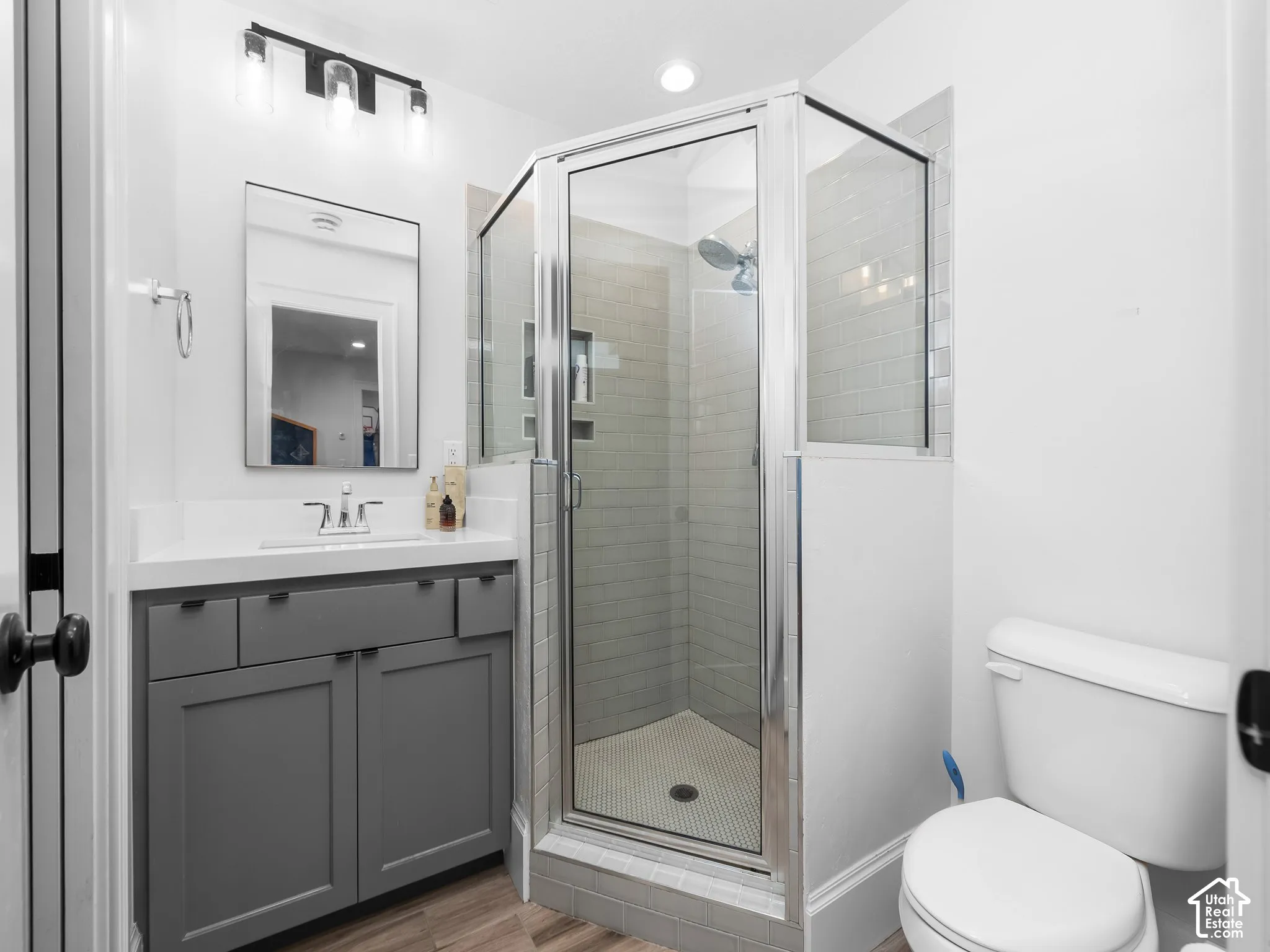 Bathroom featuring a glass-enclosed shower with subway tile, wood-finish flooring, a vanity with a white countertop, and a rectangular framed mirror