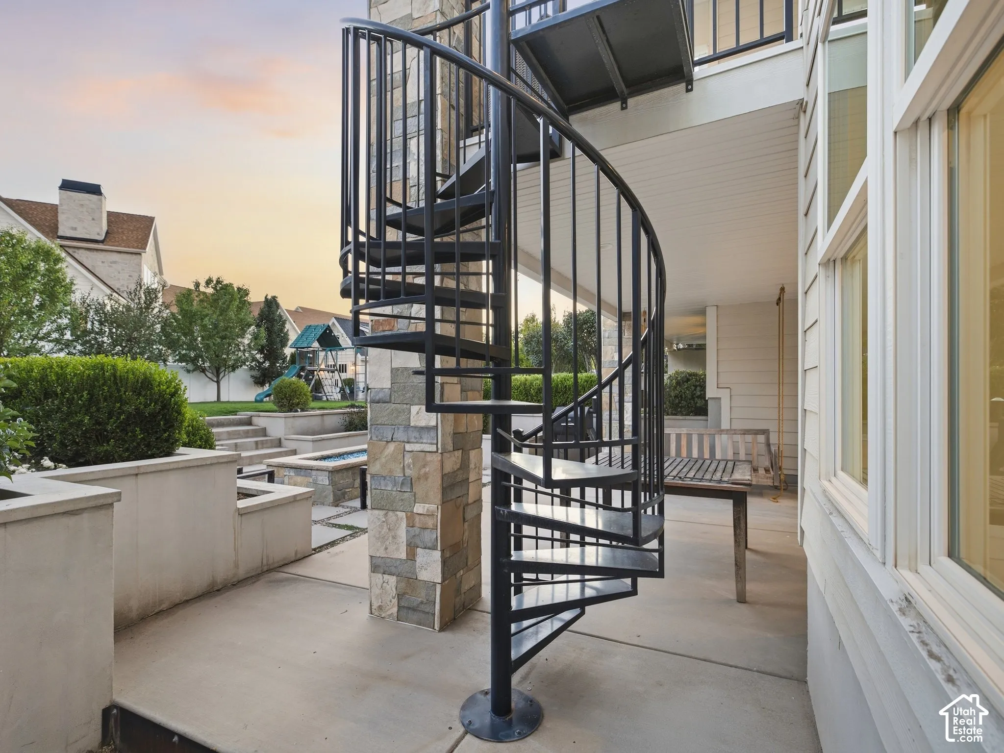 Black metal spiral staircase with stone veneer column, concrete patio, and built-in planters