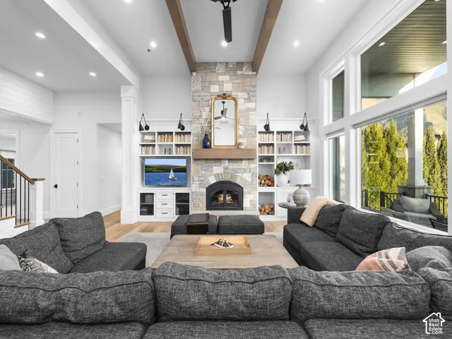 Vaulted ceilings with exposed wood beams, floor-to-ceiling stone fireplace, integrated built-in shelving, large windows, and light wood-finish flooring