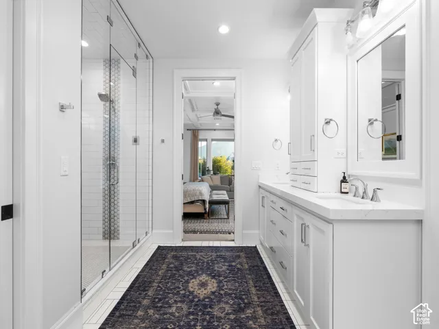 Spacious bathroom featuring a frameless glass shower, dual vanities with white cabinetry, polished chrome fixtures, and a white countertop
