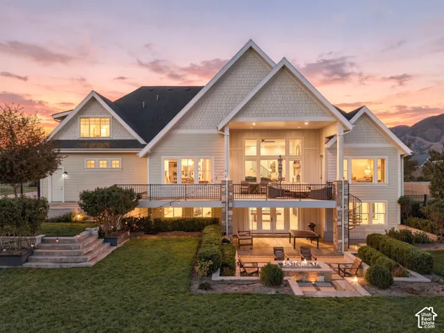 Exterior featuring multiple gables, a large upper deck with metal railings, a lower patio with a built-in fire pit, a spiral staircase, and tiered landscaping