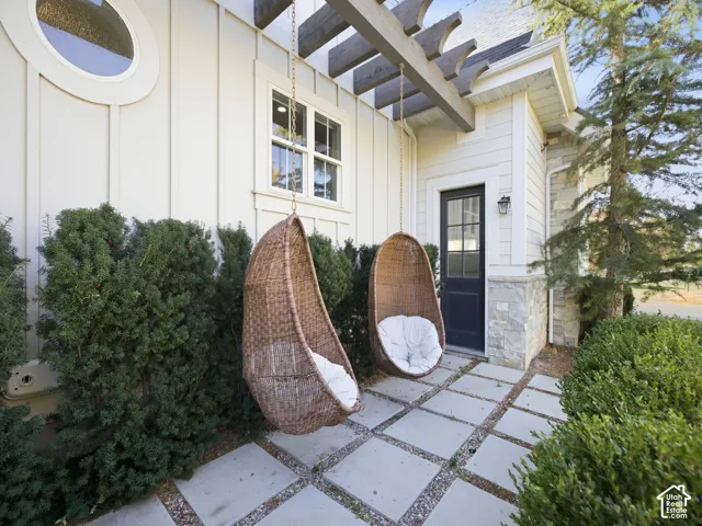 Exterior featuring a pergola structure, stone and vertical siding, a round window, and square paver patio
