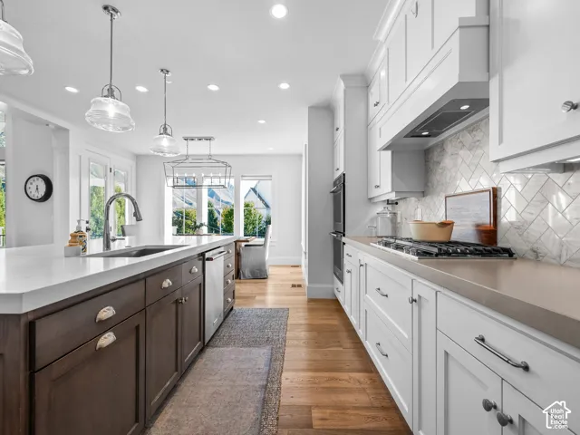 Gourmet kitchen with wood-finish flooring, white cabinetry, integrated appliances, and a central island with a stainless steel sink