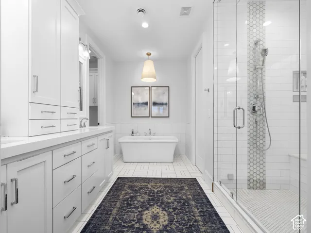 White cabinetry with chrome hardware, freestanding soaking tub, glass-enclosed shower, white subway tile, and hexagon tile accents
