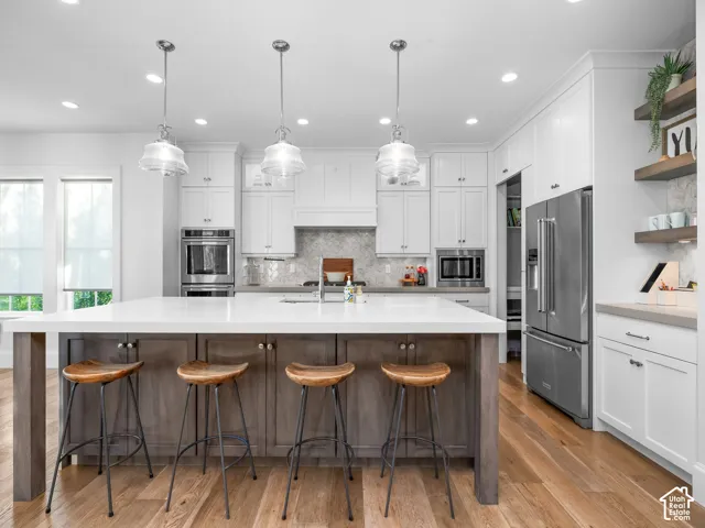 Spacious kitchen with a large central island, white cabinetry, integrated stainless steel appliances, wood-finish flooring, and pendant lighting