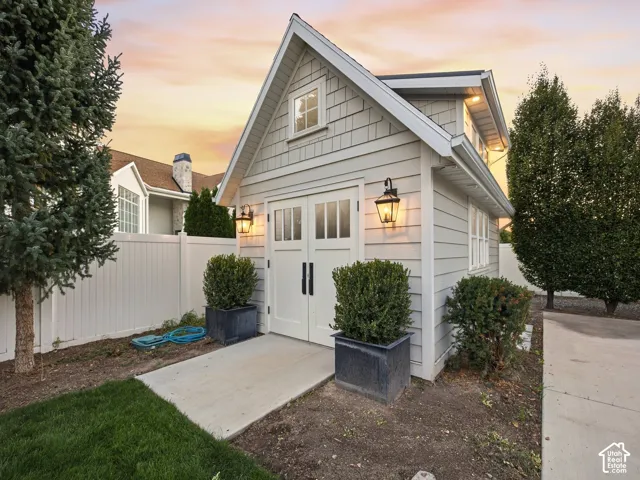 Gabled-roof outbuilding with shake and horizontal siding, featuring double doors with glass panes, transom window, and exterior wall sconces