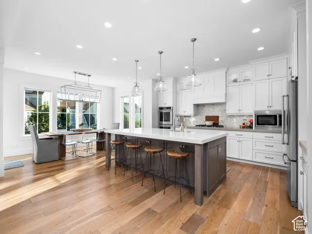 Gourmet kitchen featuring white cabinetry, a large kitchen island with counter seating, stainless steel appliances, and wood-finish flooring