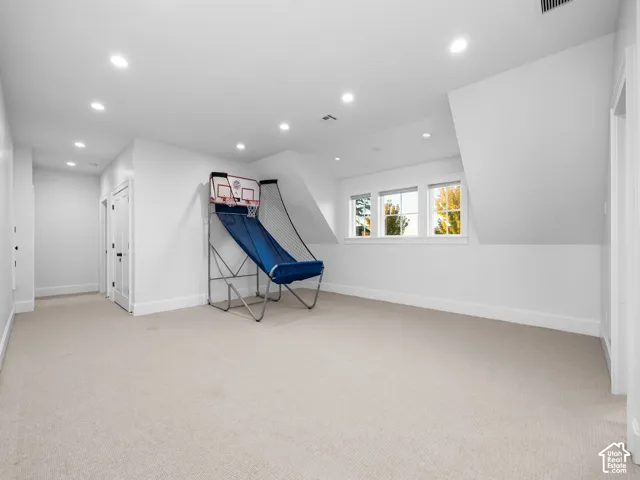 Spacious room featuring carpeting, recessed lighting, white walls, multiple windows, and a sloped ceiling