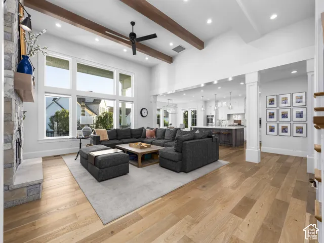 High ceilings with exposed wood beams, stone-clad fireplace with wood mantel, light wood-finish flooring, recessed lighting, and expansive windows
