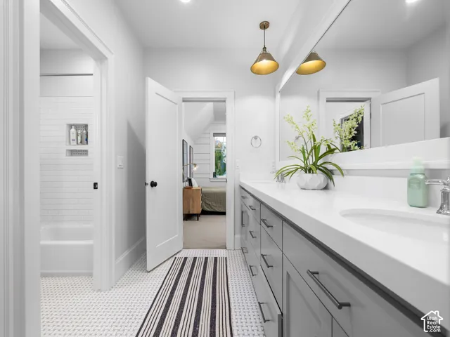 Double vanity with a white countertop and integrated sinks, gray shaker-style cabinetry with matte black hardware, and two brass-finish pendant lights