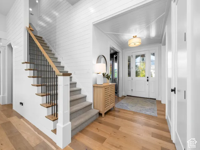 Hardwood flooring, shiplap wall finishes, shiplap ceiling details, glass-paneled entry door, and a staircase with a carpet runner and wrought iron balusters