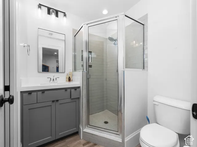 Bathroom featuring a glass-enclosed shower with subway tile, wood-finish flooring, a vanity with a white countertop, and a rectangular framed mirror